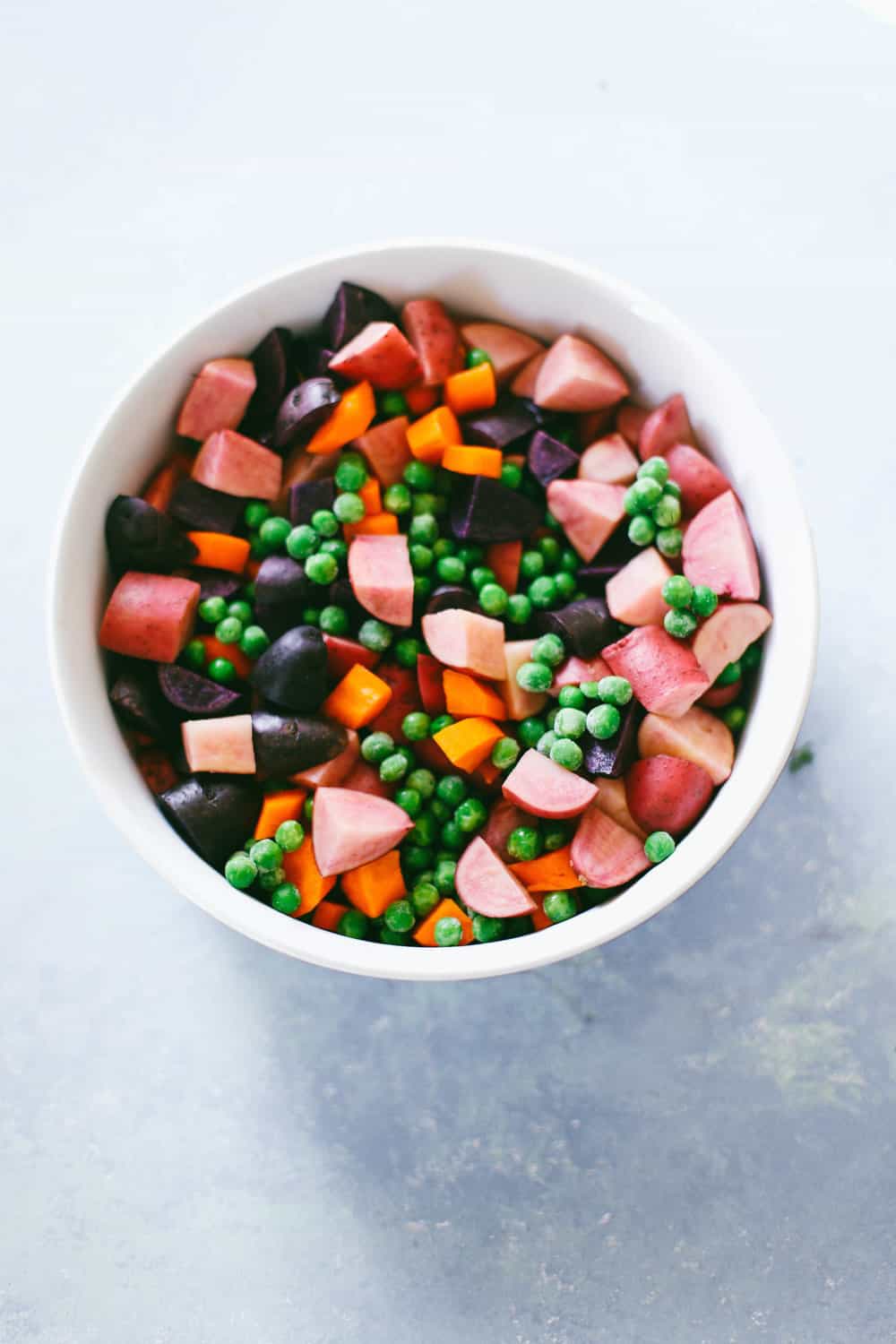 chopped potatoes, carrots and peas in white bowl