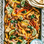 chili lime chicken and vegetables on a sheet pan with flour tortillas on the side