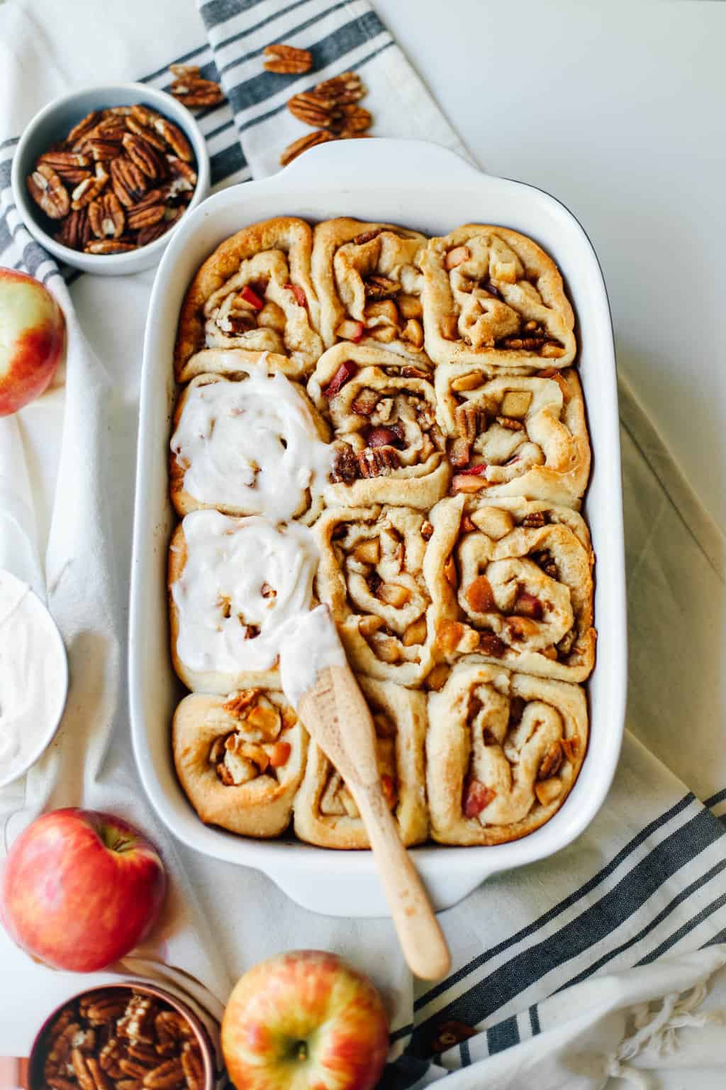 A casserole dish of Apple Pecan Cinnamon Rolls with icing.