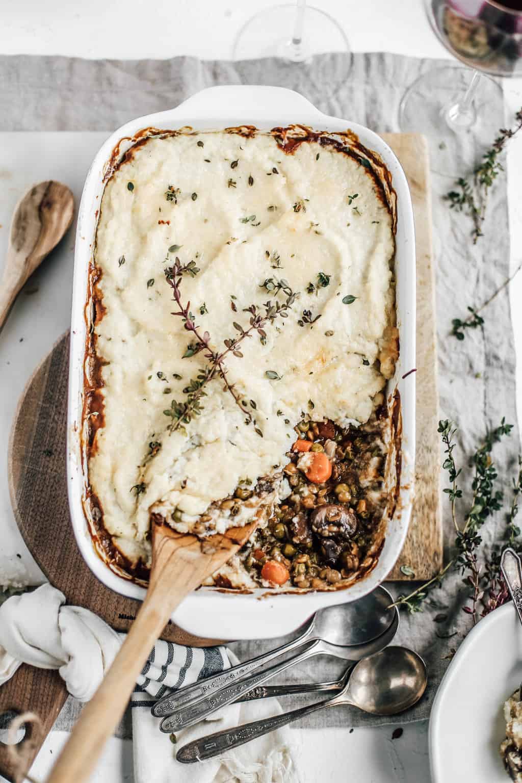 A casserole dish of Vegetarian Shepherds Pie with Lentils and a wooden spoon.