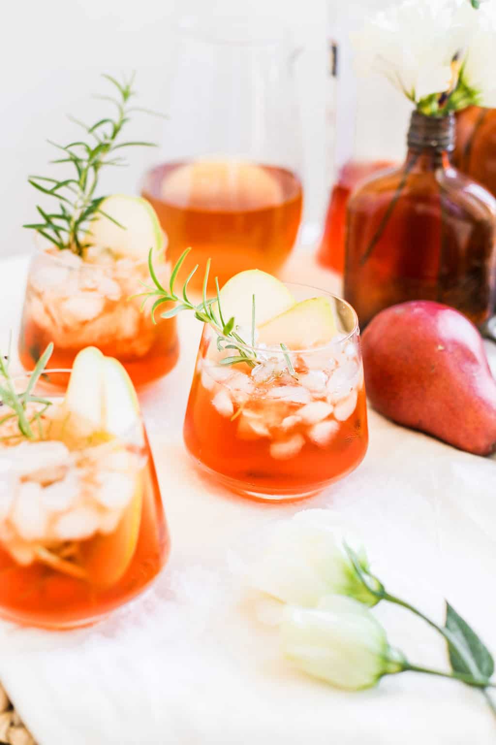 A low clear glass filled with aperol and hard cider with a rosemary sprig.