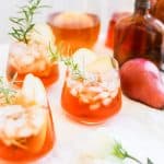 A low clear glass filled with aperol and hard cider with a rosemary sprig.