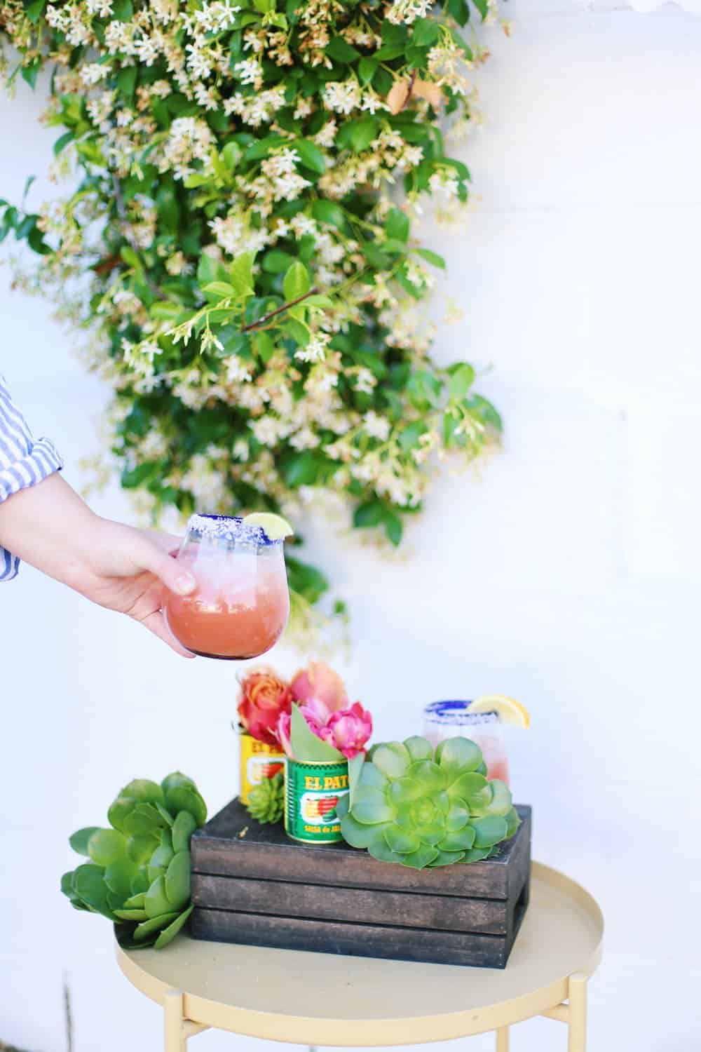 A hand holding a margarita on the rocks with flowers in the background