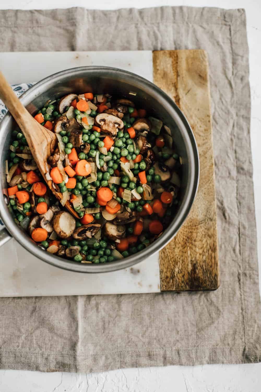 Diced carrots, onions, peas, and mushrooms being sauteed in a pan. 