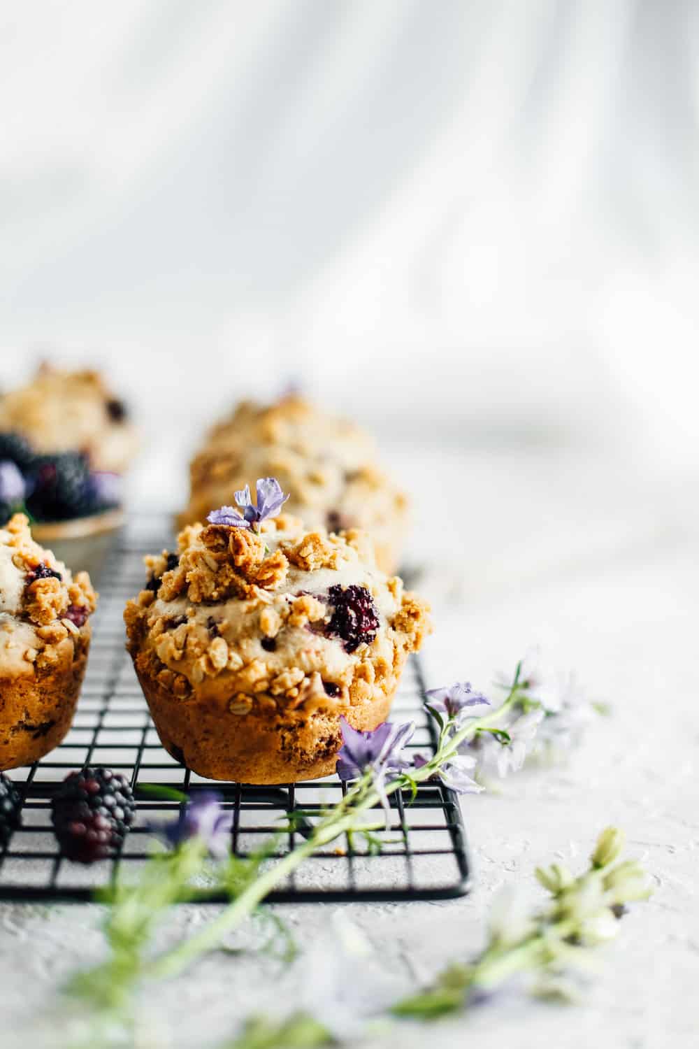 blackberry muffins on a black cooling rack with a sprig of herbs in front of them