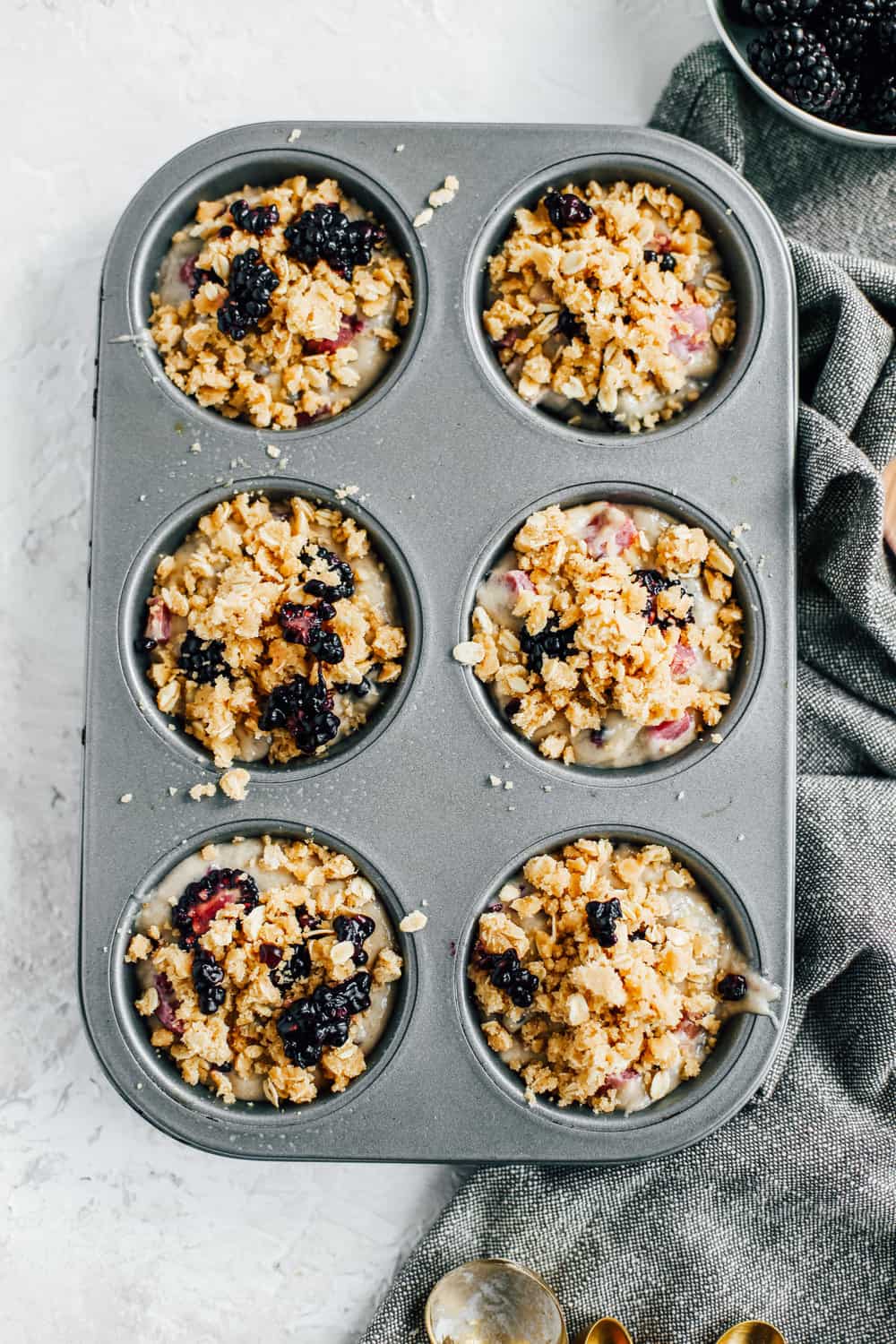 a muffin tin full of the muffin batter topped with oat crumble and fresh fruit