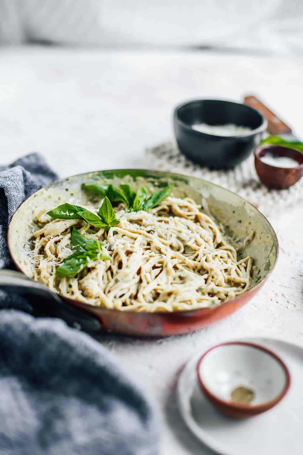 Skinny Fettuccine Pesto Alfredo in skillet with basil leaves and bowl of Parmesan cheese