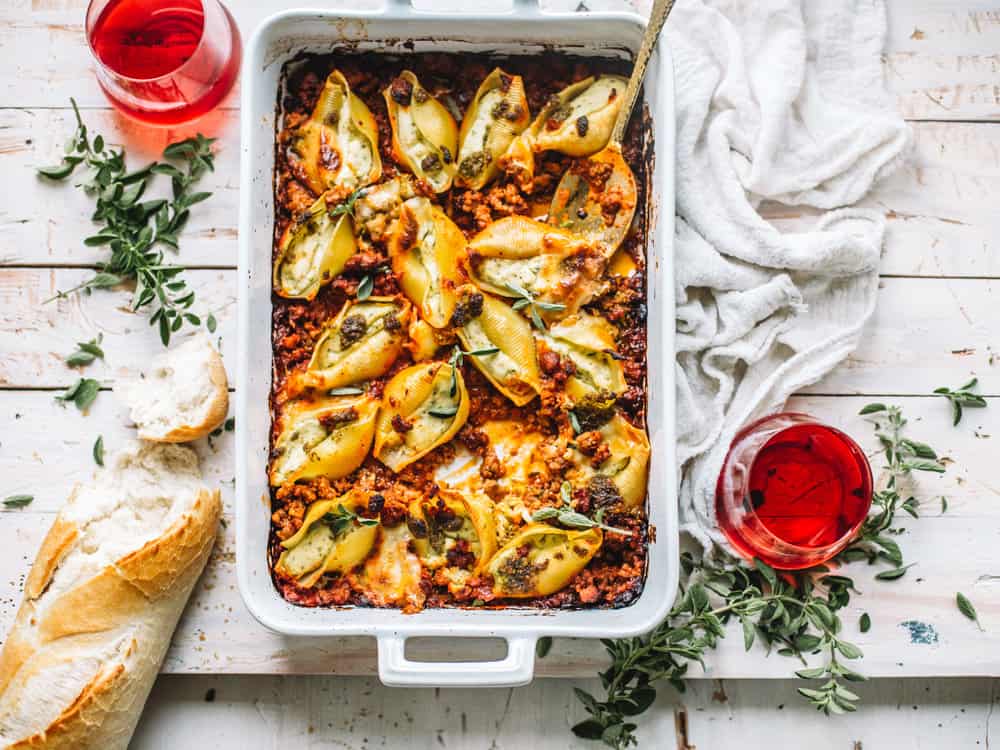 pesto stuffed shells with Italian sausage meat marinara in white casserole dish on white kitchen towel with spoon