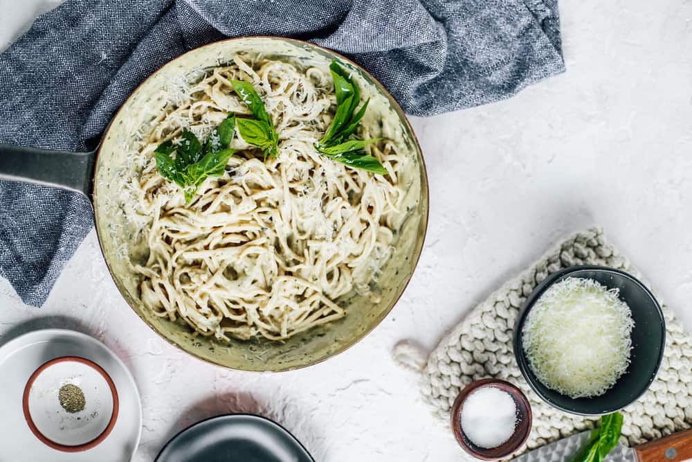 Skinny Fettuccine Pesto Alfredo in skillet with basil leaves and bowl of Parmesan cheese