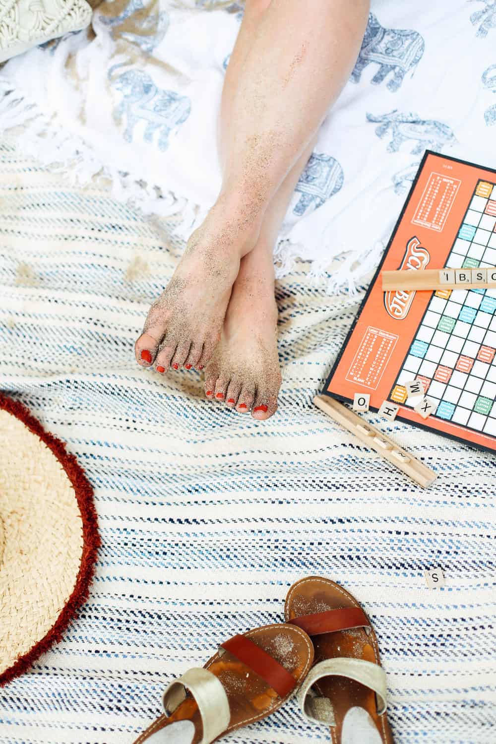 Sandy bare feet with Scrabble game board on beach towels