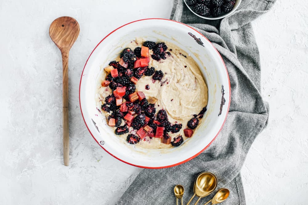 a bowl of the muffin batter with chunks of blackberries and rhubarb beside a wooden spoon