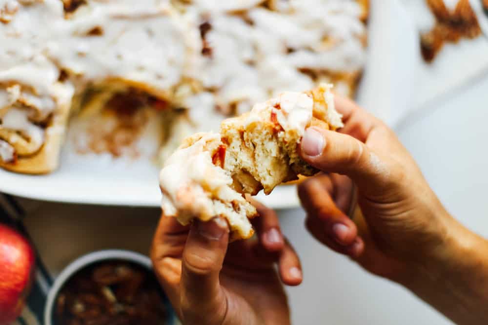 A apple pecan cinnamon roll being ripped apart. 