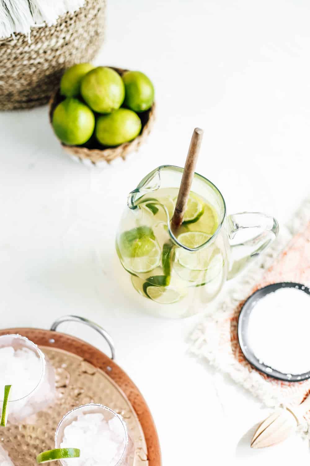 A pitcher of a classic margarita with limes and a wooden spoon. 