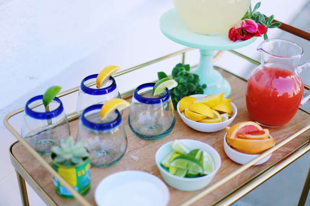 Cocktail glasses lemons limes and grapefruit wedges in white bowls and pitcher of juice on a bar cart