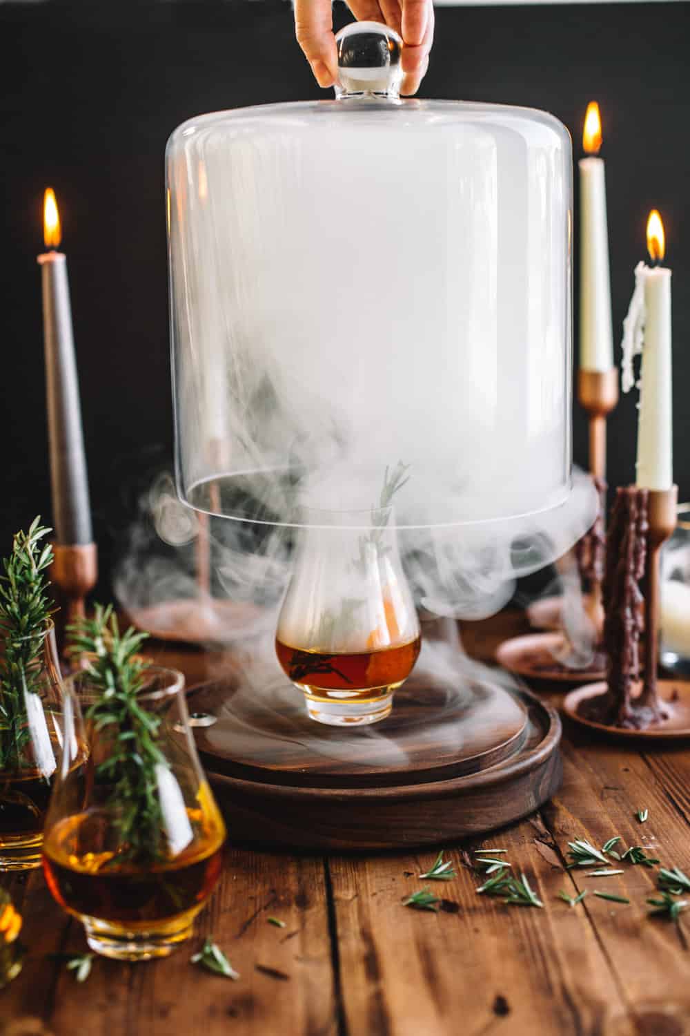 Smoking Cloche being lifted with a glass of Goblet of Fire garnished with a sprig of rosemary. 