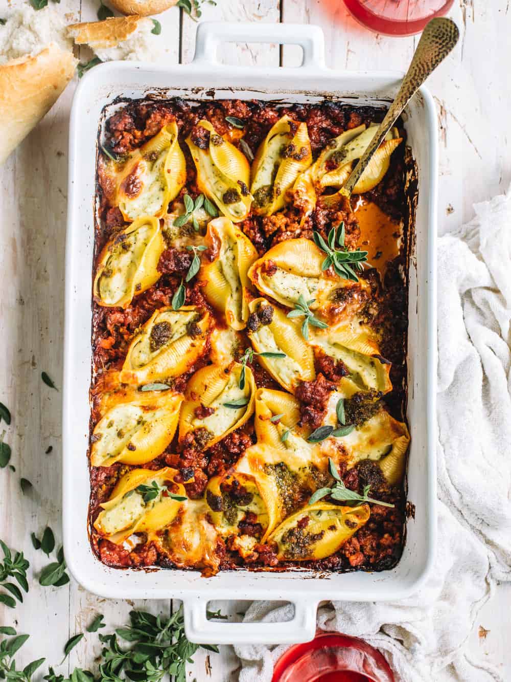 pesto stuffed shells with Italian sausage meat marinara in white casserole dish on white kitchen towel with spoon