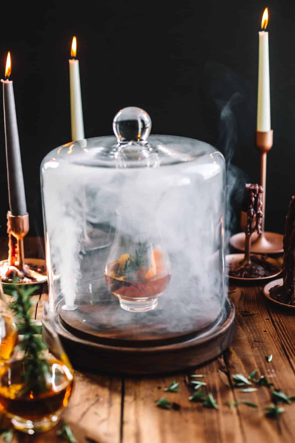 Smoking Cloche being lifted with a glass of Goblet of Fire garnished with a sprig of rosemary. 