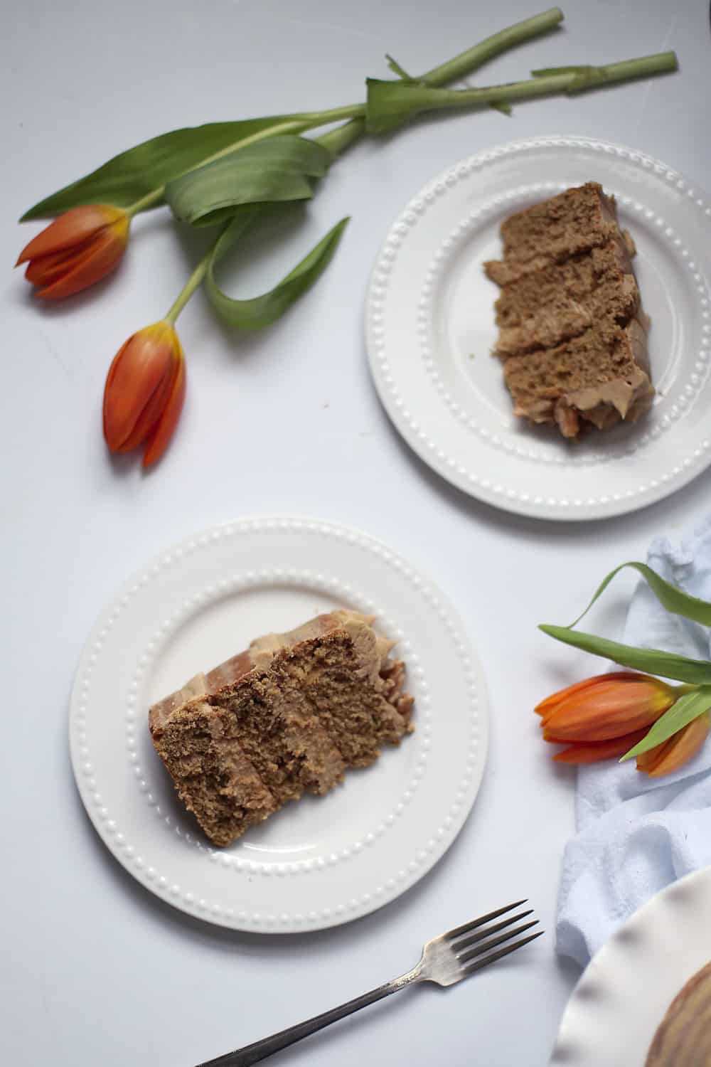 two slices of coffee walnut cake on white plates with orange tulips. 