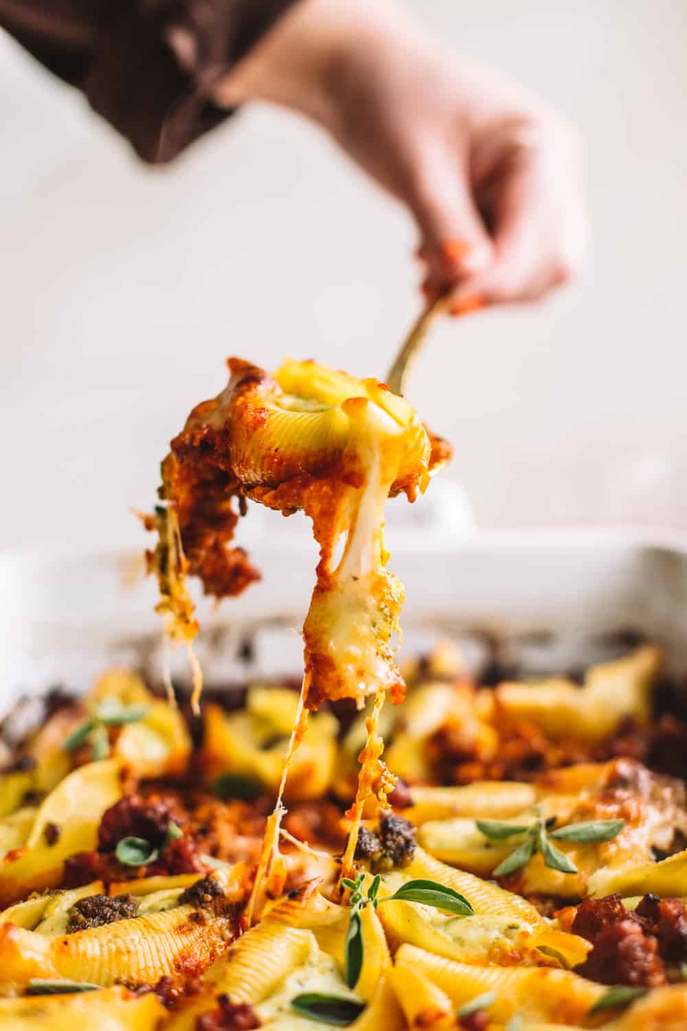 cheesy pesto stuffed shells being spooned out from casserole dish