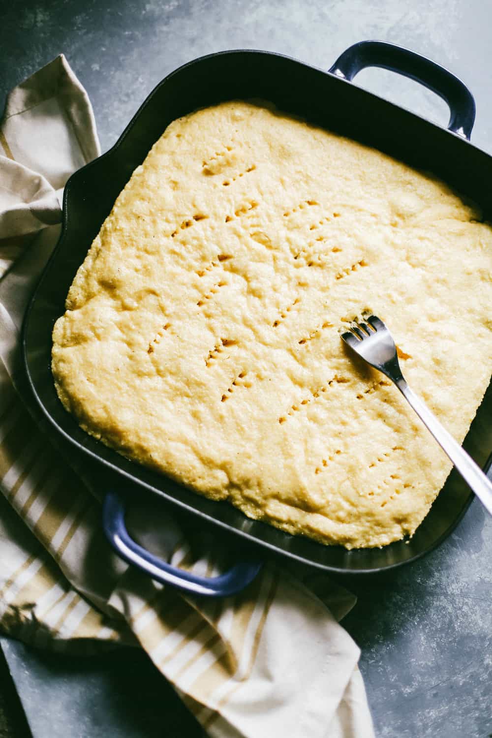 A casserole with baked cornbread, a fork poking through the cornbread. 