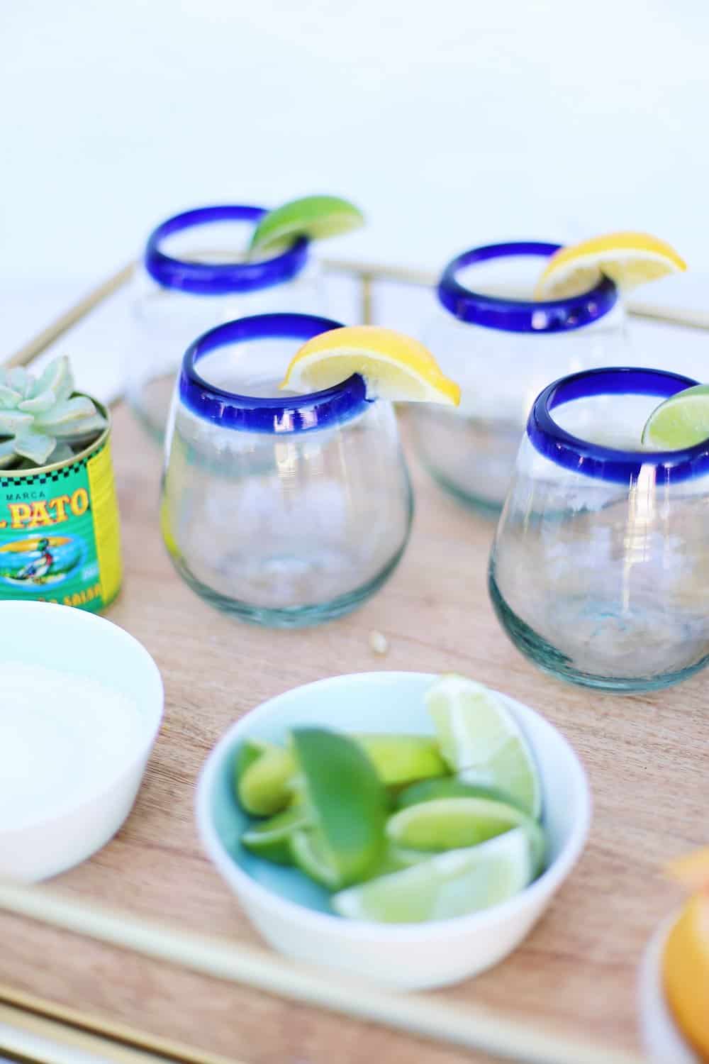 Cocktail glasses garnished with lemon and limes with limes in a white bowl