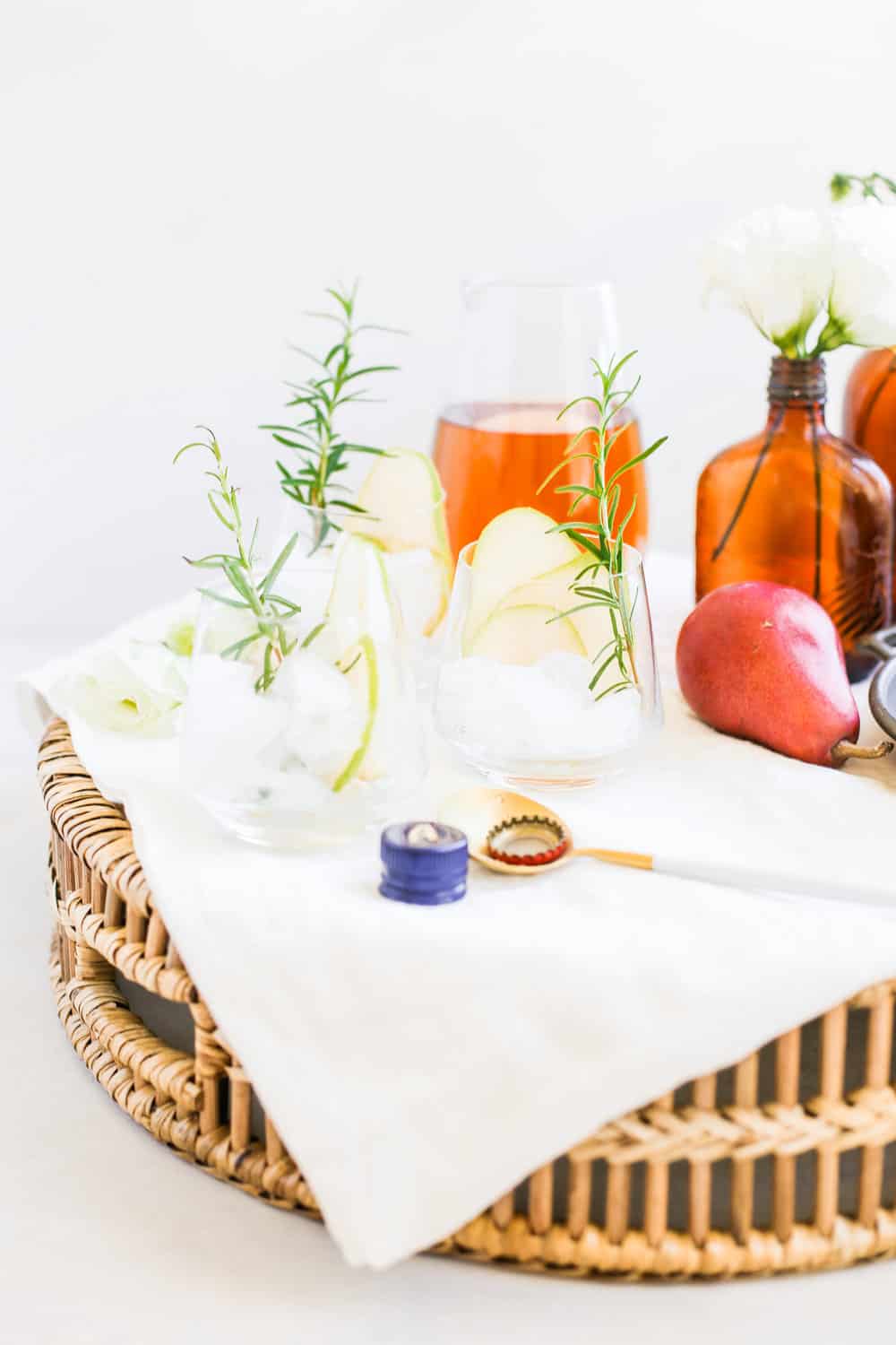 Low clear glasses garnished with a sliced pear, a sprig of rosemary, and ice on a serving tray. 