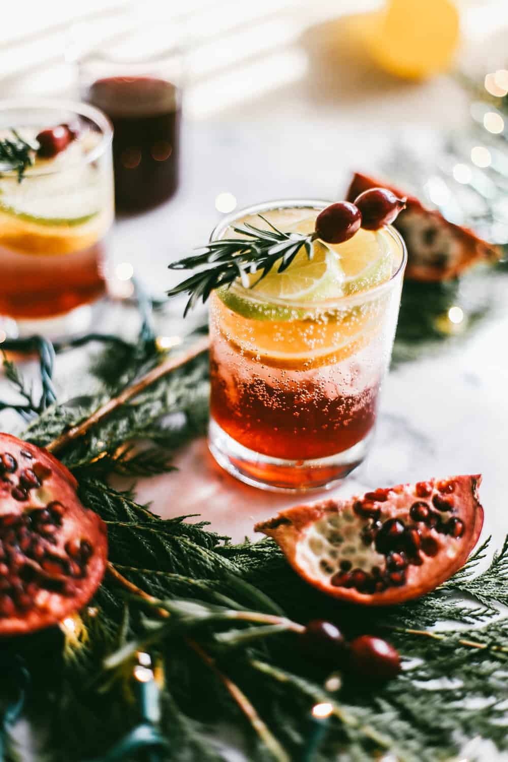 Low glass filled with pomegranate juice and champagne garnished with orange slices, rosemary and cranberries.