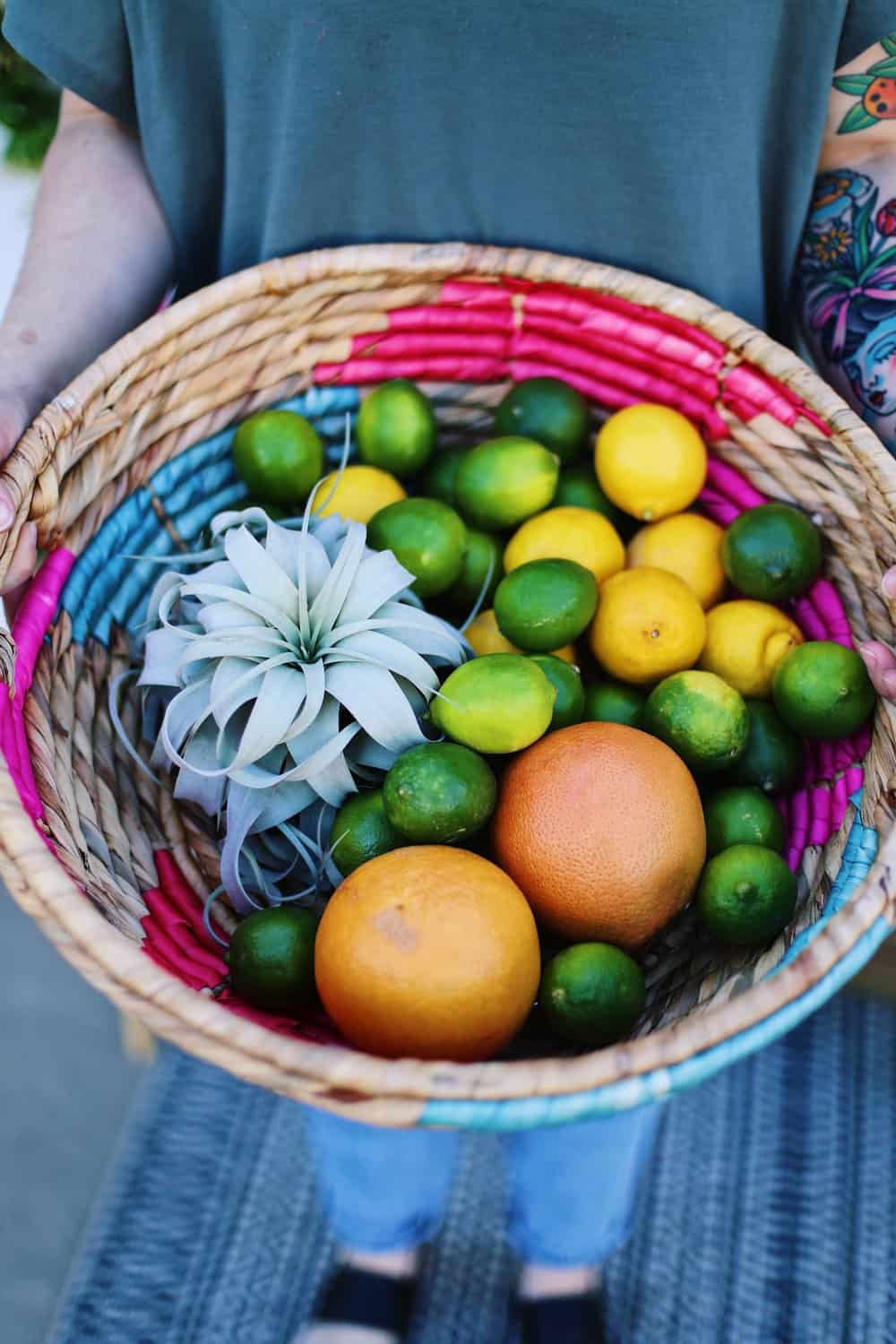 Two hands holding a wicker basket full of grapefruit lemons and limes