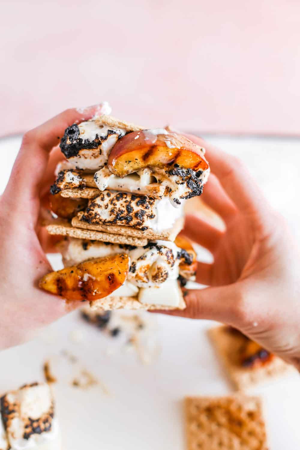 Two hands with a stack of three Smeaches with grilled peaches, toasted marshmallows, white chocolate, and graham crackers