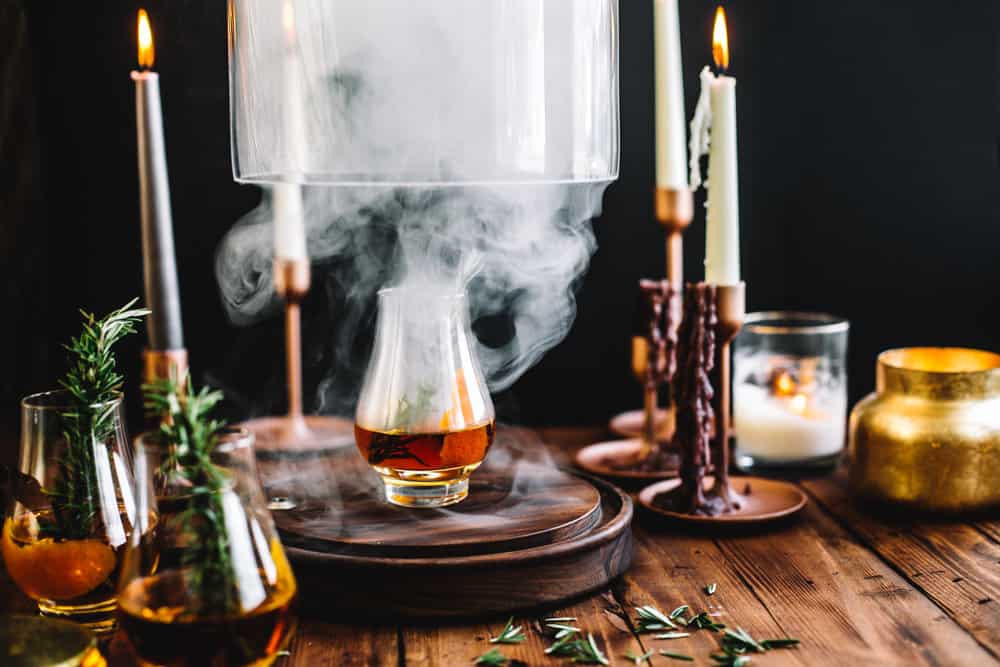 Smoking Cloche being lifted with a glass of Goblet of Fire garnished with a sprig of rosemary. 