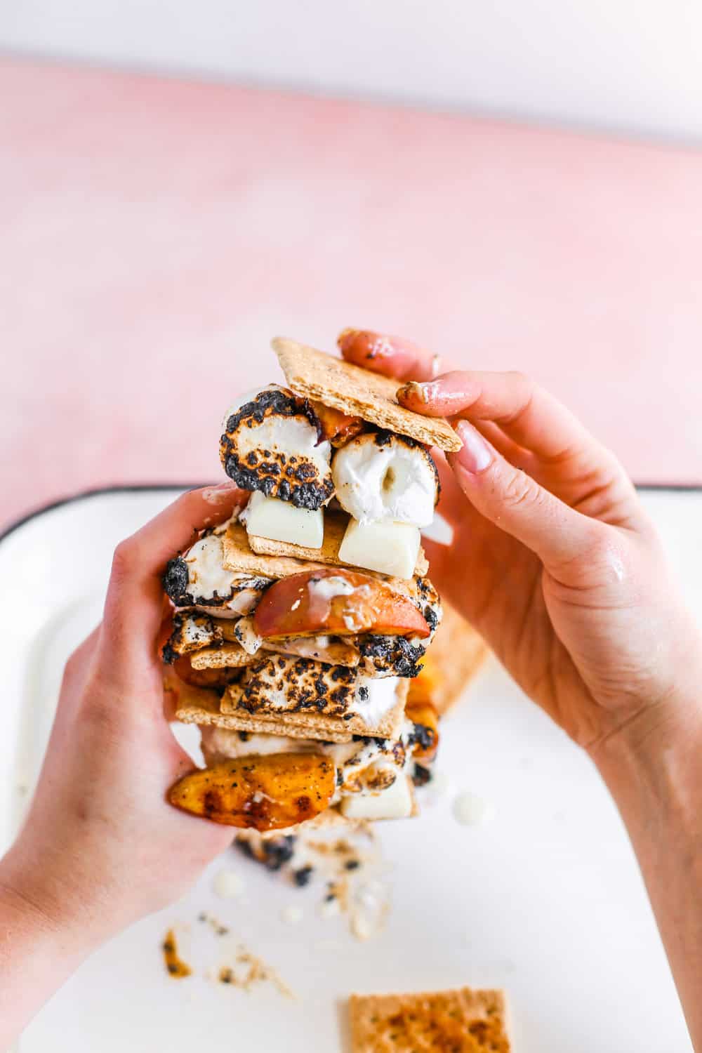 Two hands holding a stack of three Smeaches with grilled peaches, white chocolate, toasted marshmallows, and graham crackers