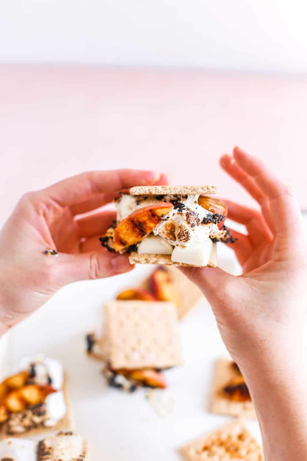 Two hands holding one Smeaches with grilled peaches, white chocolate, toasted marshmallows, and graham crackers