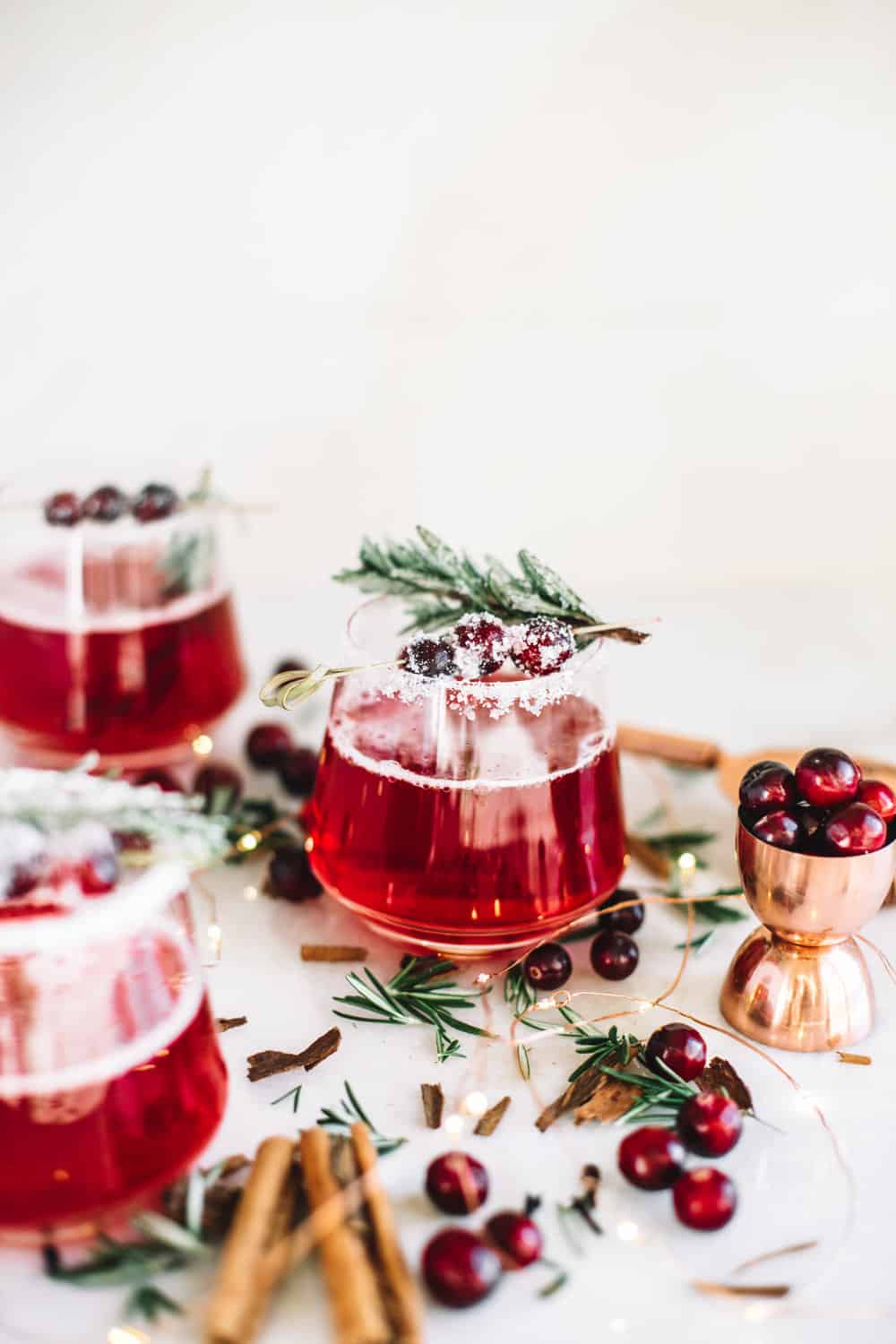 Low glass filled with a cranberry whiskey cocktails garnished with frosted cranberries and a rosemary sprig.