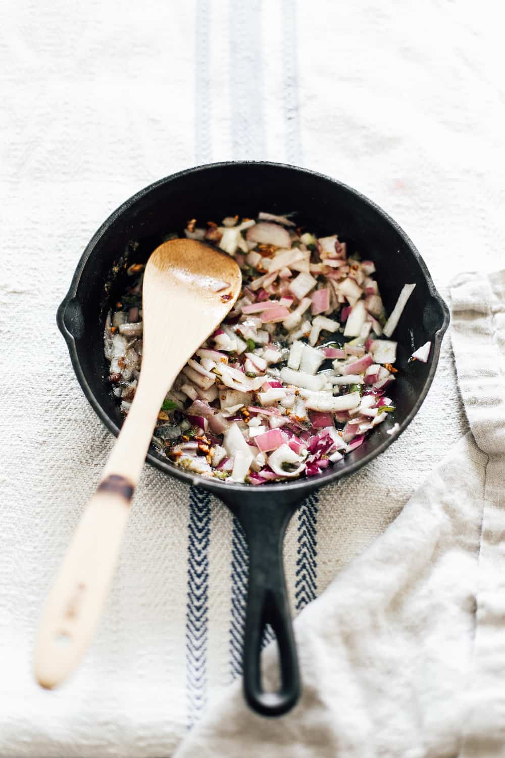 A skillet with sautéed red onions and a wooden spoon