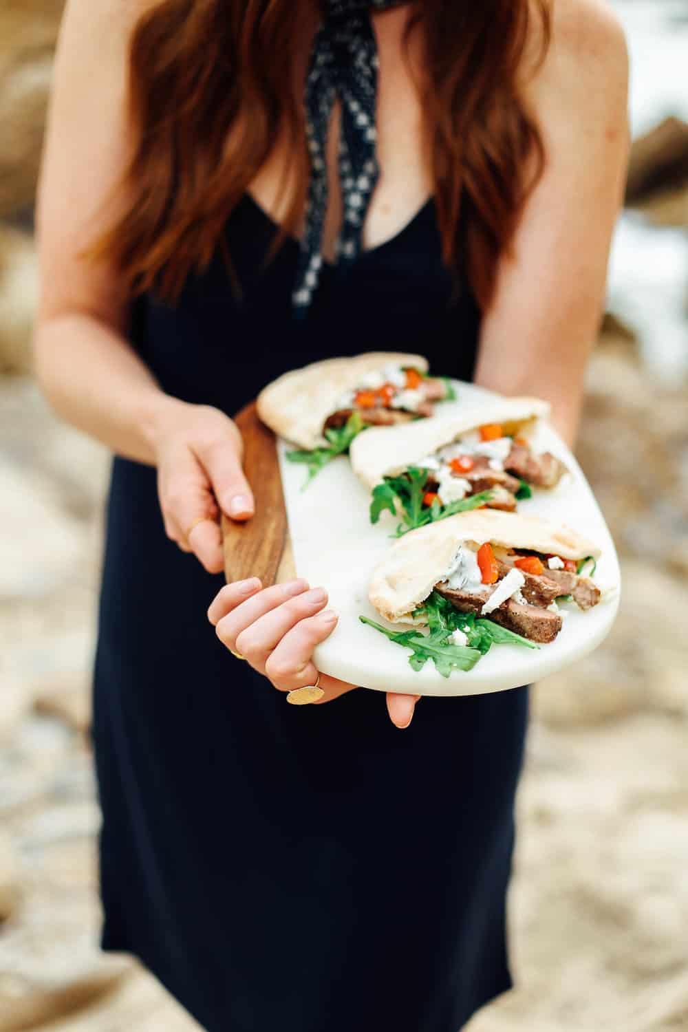 Elizabeth holding Garlic Lamb Pita Pockets on a cutting board on the beach