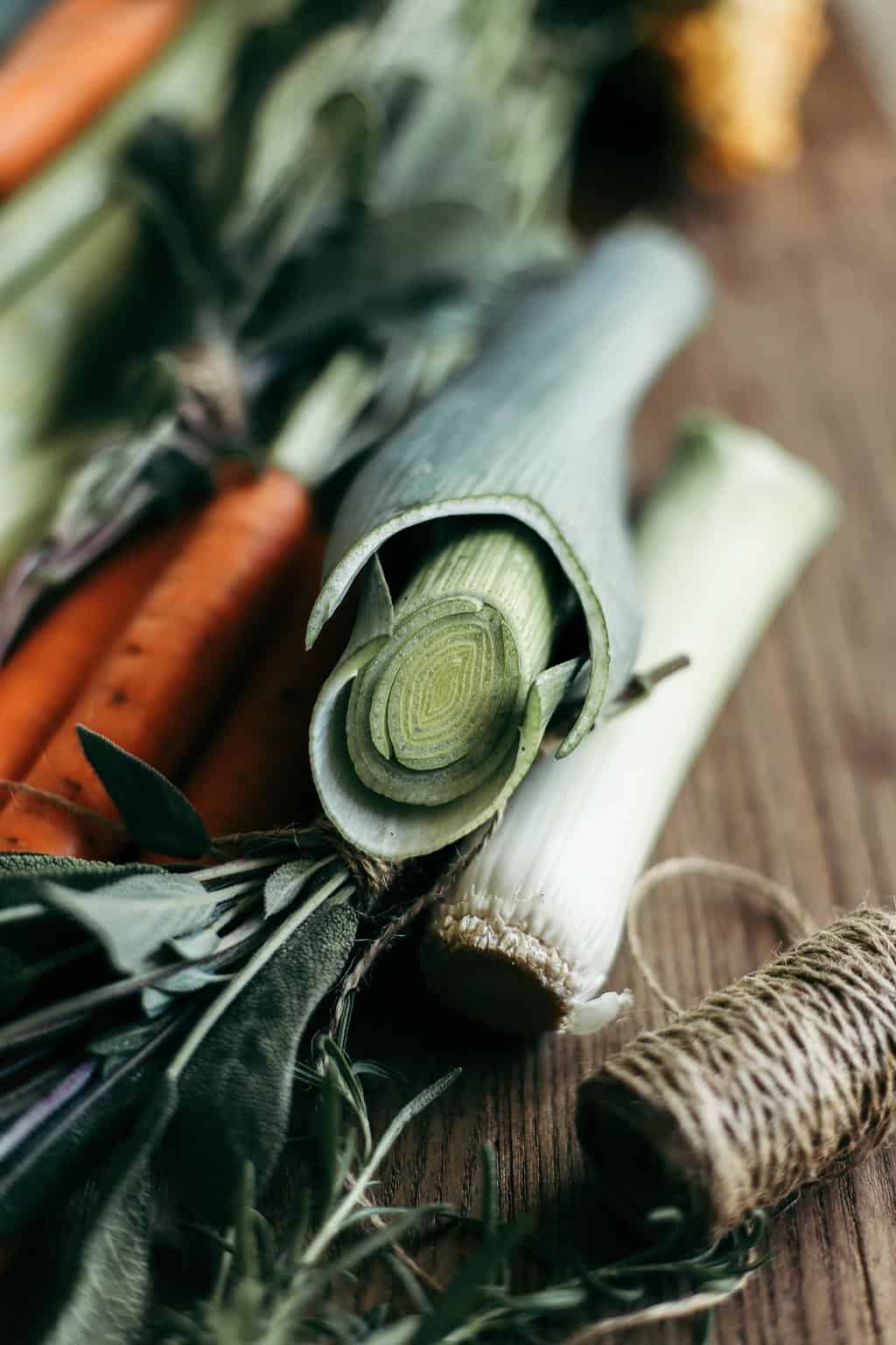 Carrots, celery, sage, and leeks on a wooden cutting board. 