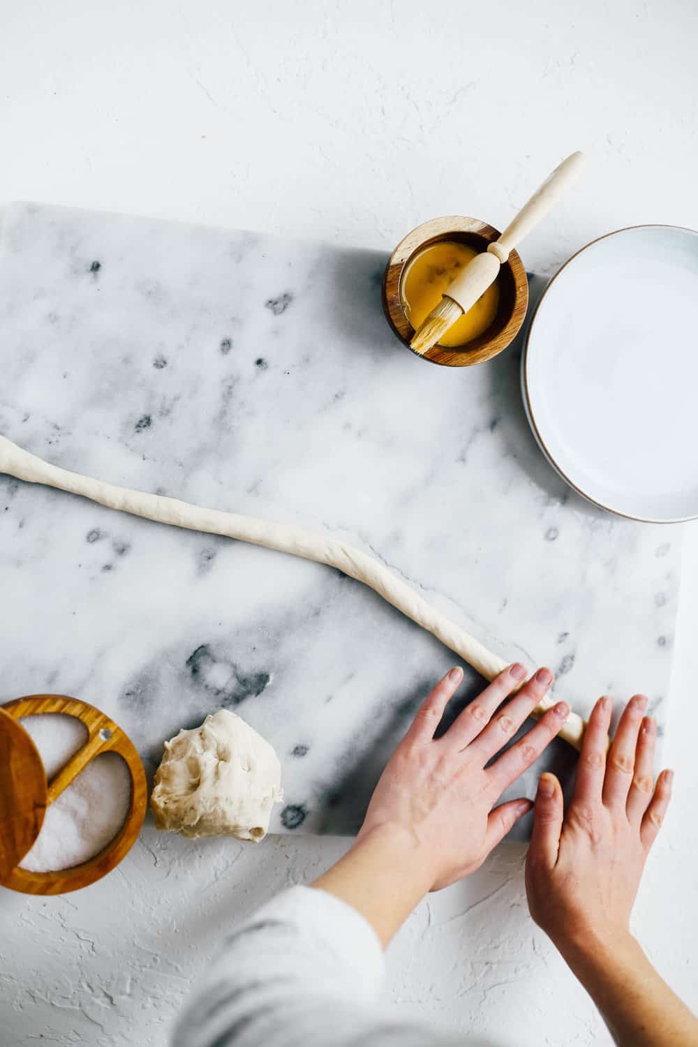 two hands rolling pretzel dough on marble countertop