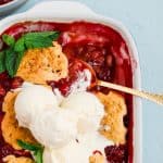 a casserole dish full of cherry rhubarb cobbler topped with vanilla ice cream