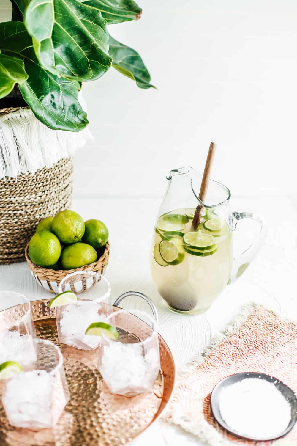 A pitcher of a classic margarita with limes and a wooden spoon.