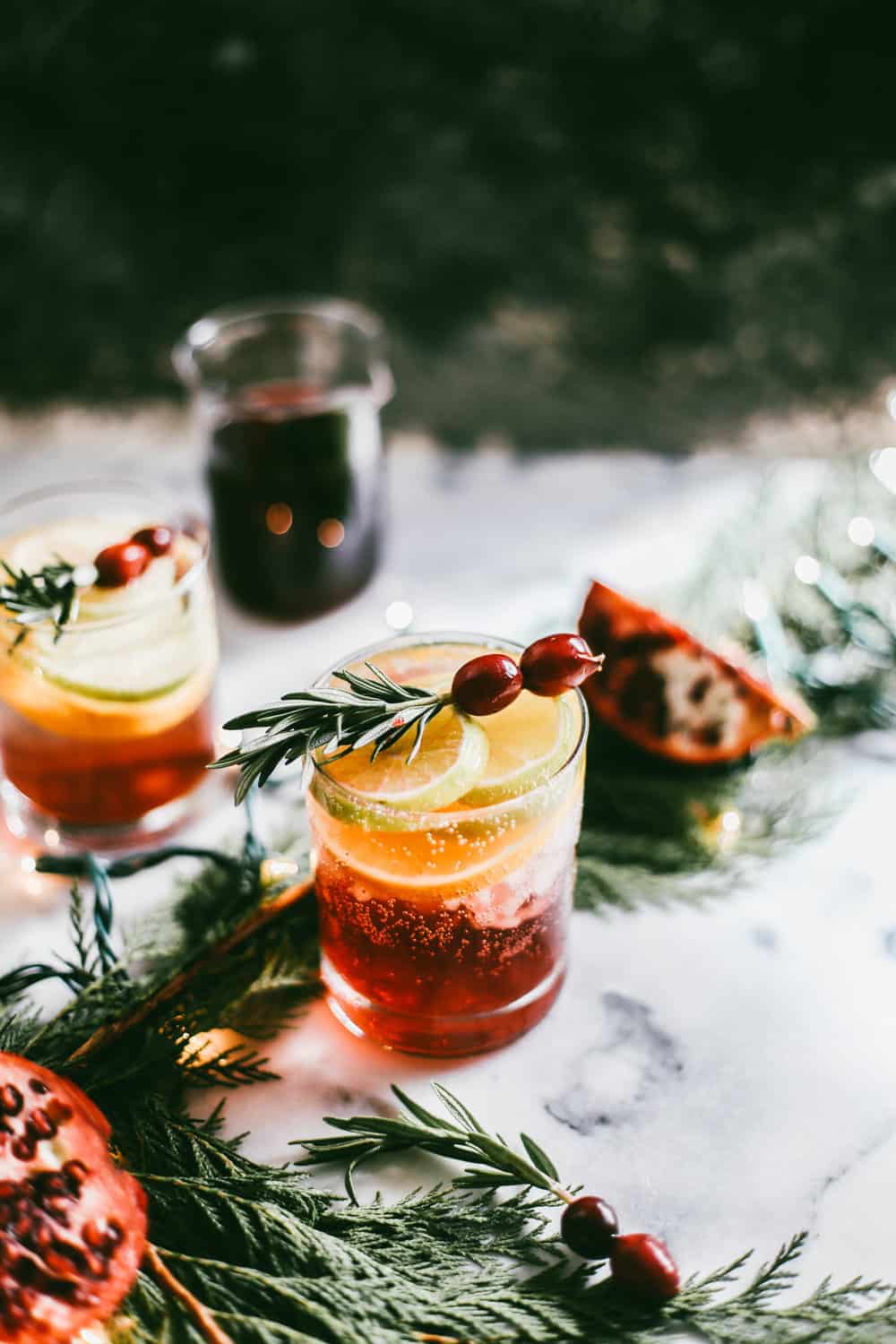 Low glass filled with pomegranate juice and champagne garnished with orange slices, rosemary and cranberries.