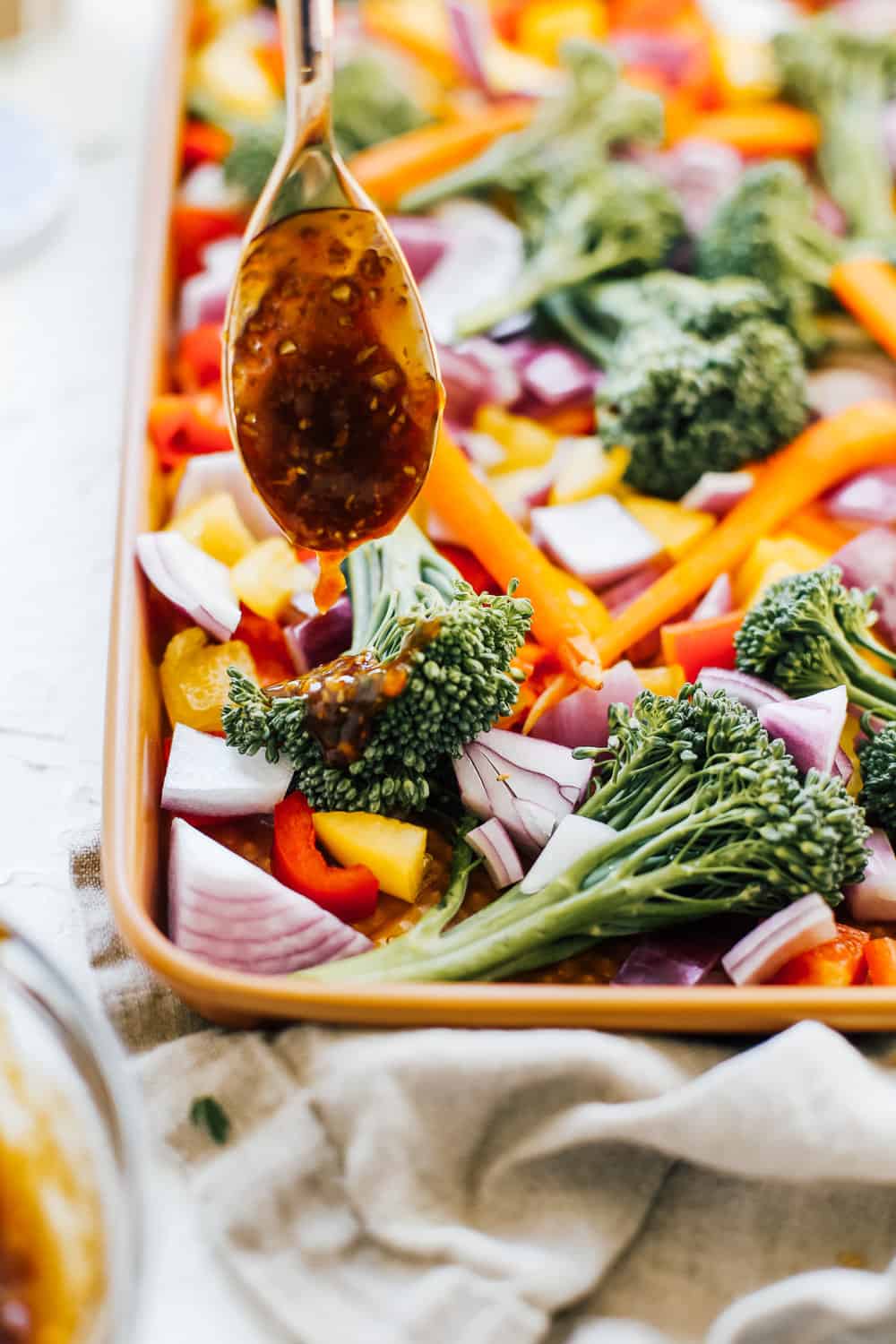 Asian style glaze spooning over broccolini, carrots, peppers, onions on sheet pan