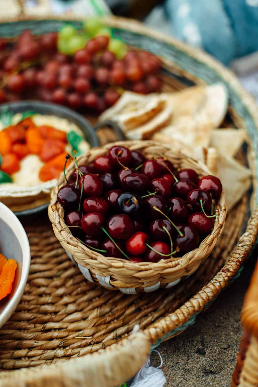 Cherries in a picnic bowl with pita hummus and grapes in a wicker basket