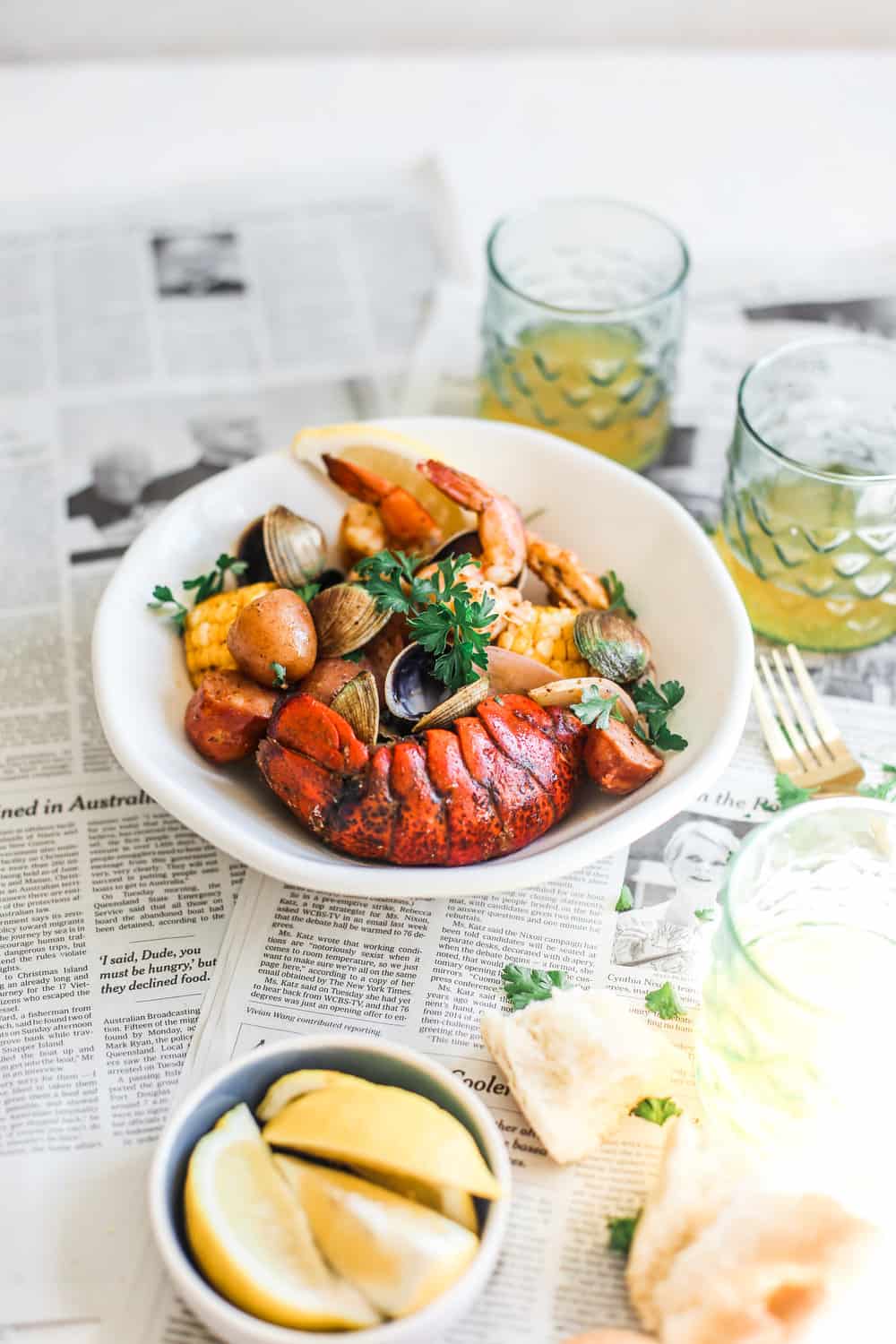 lobster tails, shirmp and clams in white bowl with lemon wedges