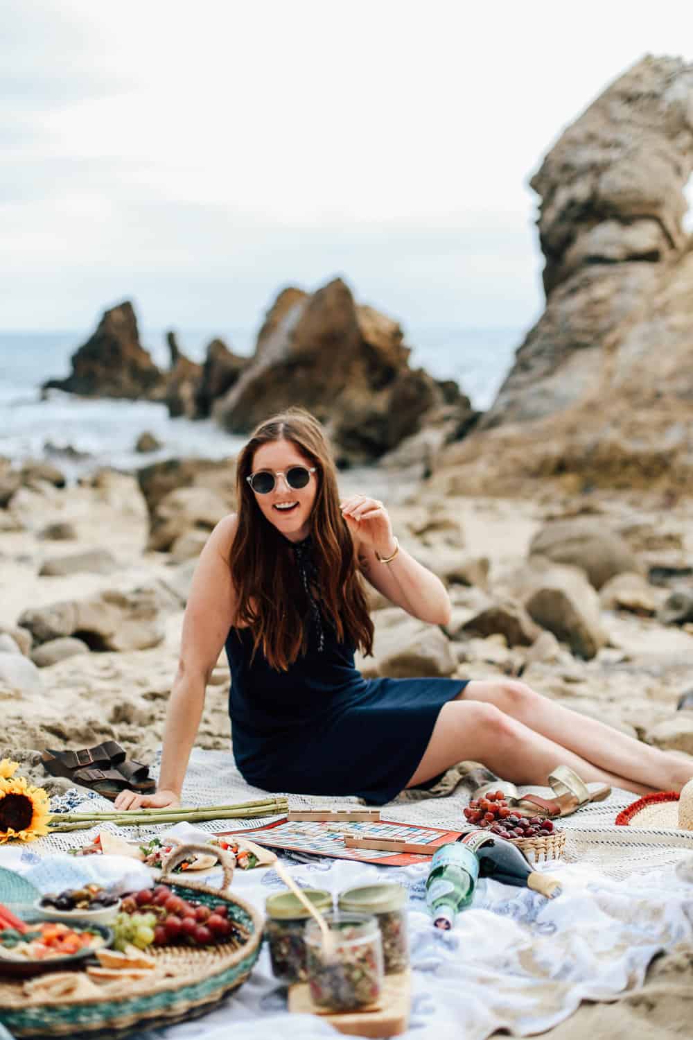 Elizabeth sitting on beach towels with beach food and Scrabble game board on the beach