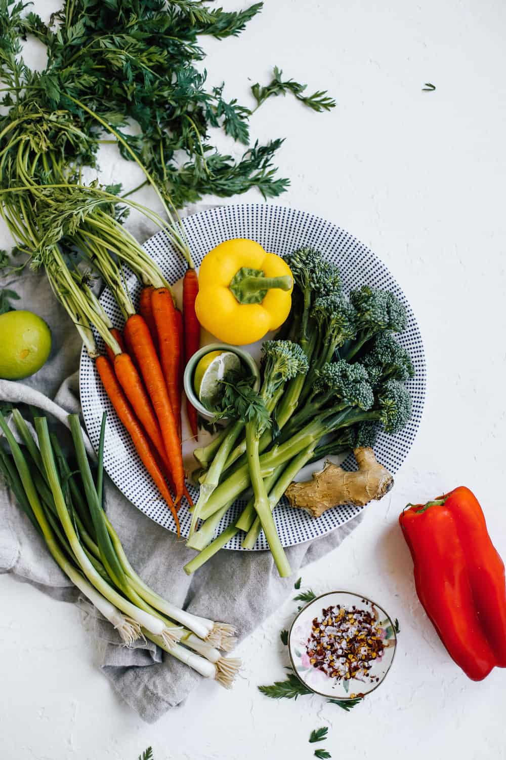 yellow bell pepper, carrots, broocolini in white bowl with green onions