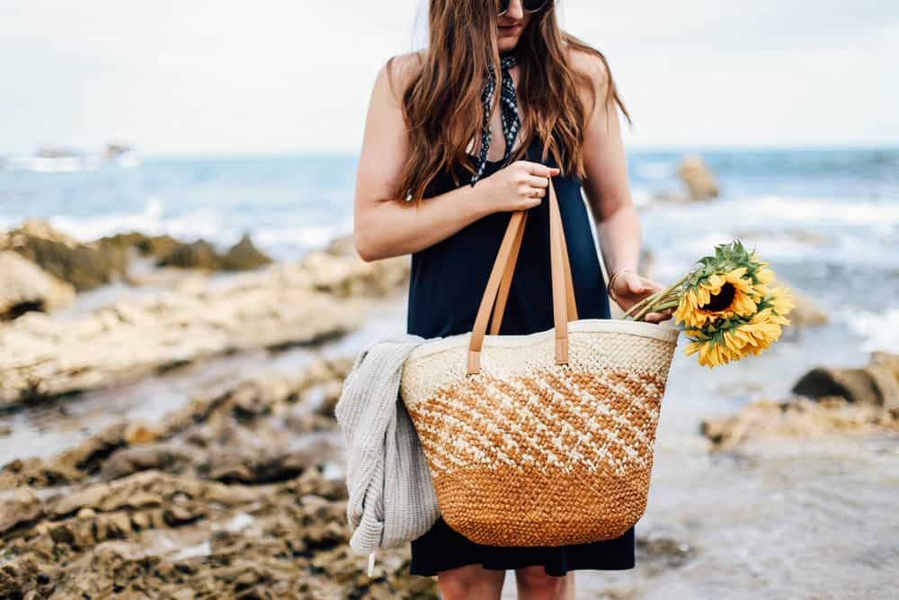 Elizabeth carrying a beach bag with sunflowers on the beach