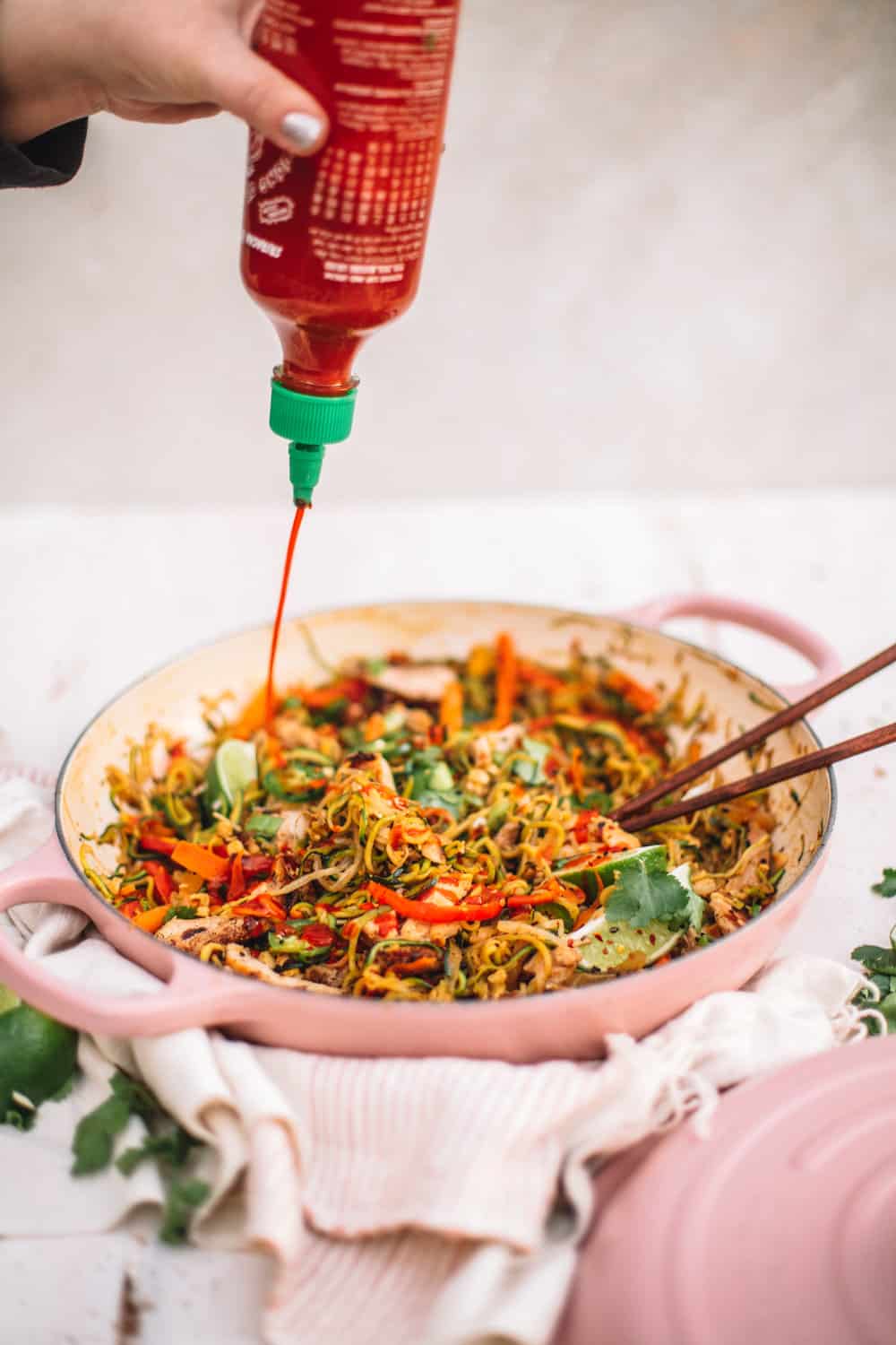 Healthy Chicken Pad Thai with Zoodles in a pan with hot sauce being squirted. 