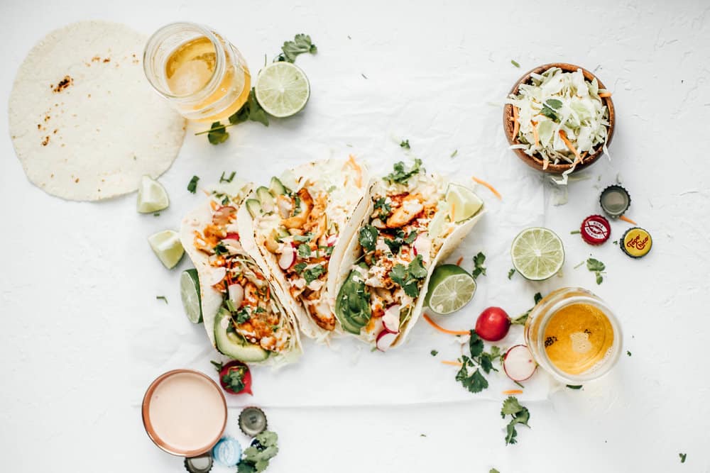 Three blackened cod tacos with a bowl of cabbage and two glasses of beer. 