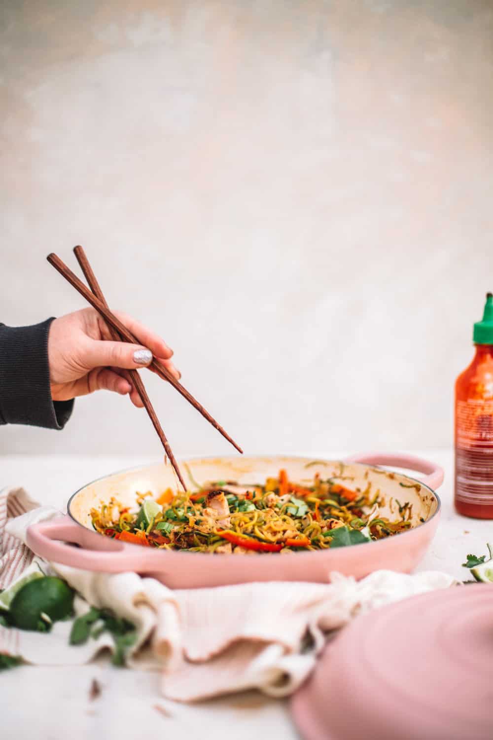 Healthy Pad Thai in a pink pan with a hand holding chopsticks. 