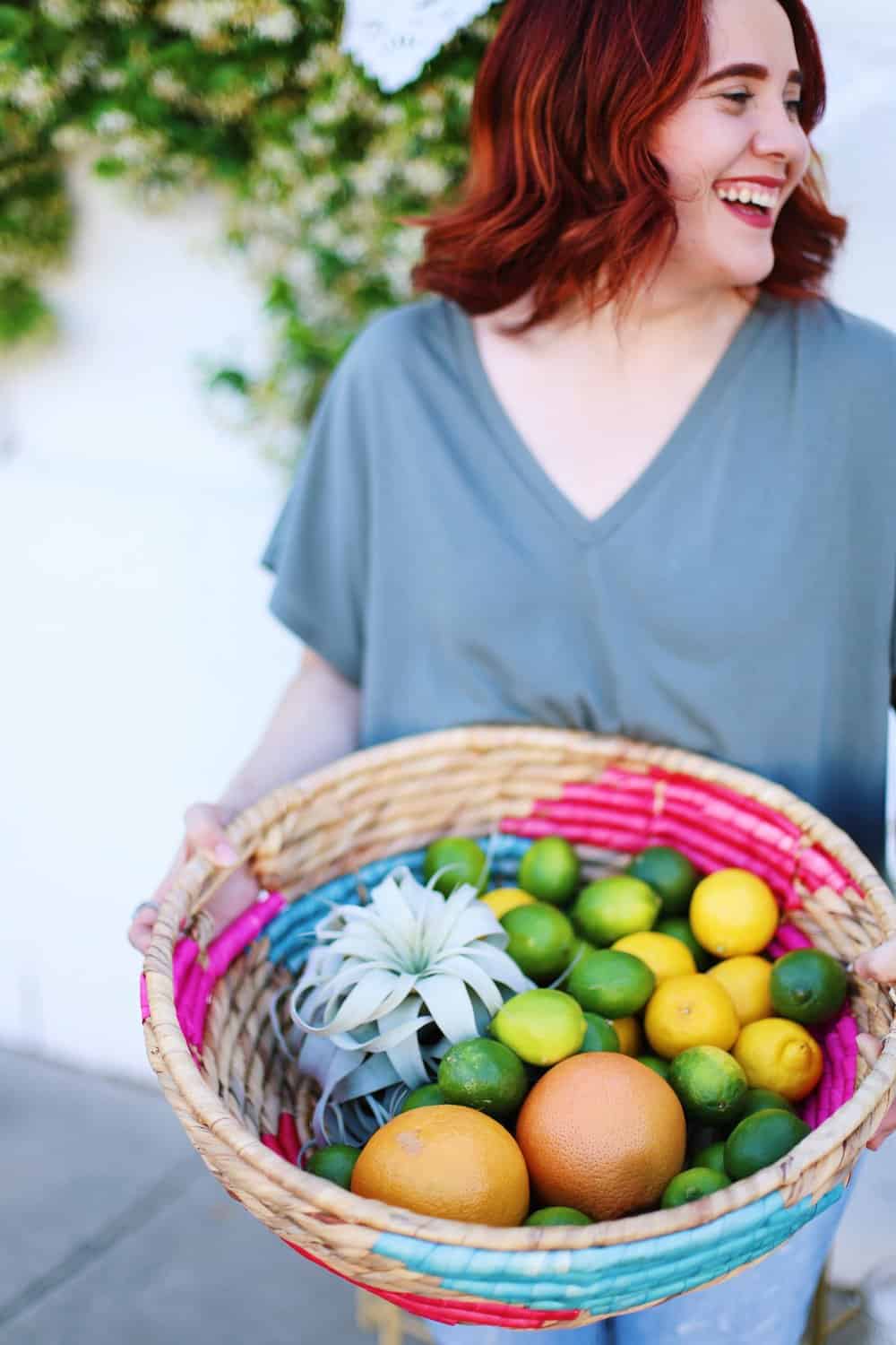 Two hands holding a wicker basket filled with grapefruits lemons and limes